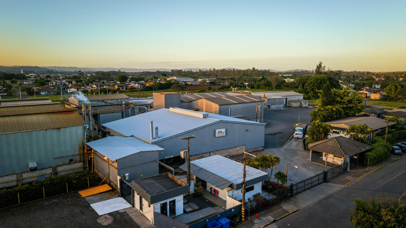 Vista da planta industrial da Sul Óxidos em dia claro, com torre de processo, silos e área verde